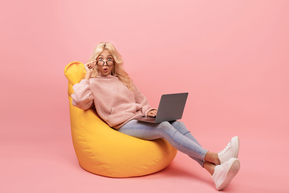 Deadline Concept. Emotional Freelancer Woman Sitting In Bean Bag Chair With Laptop Computer And Touching Glasses