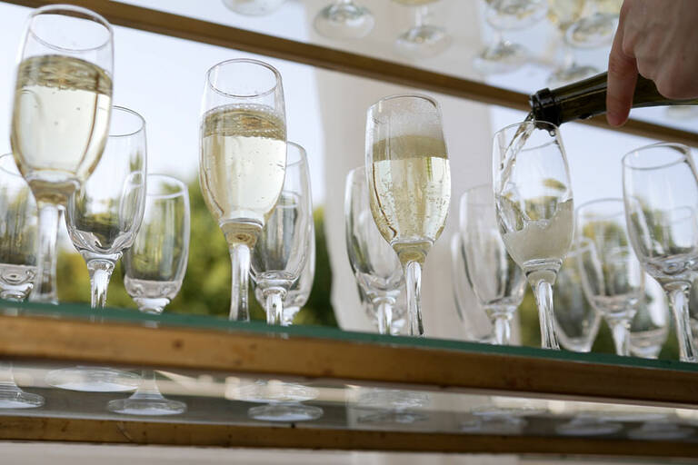 A Bottle Of Sparkling Champagne And Glasses Are Poured Into A Glass At An Outdoor Wedding Event. Open Catering, Champagne Is Poured Into A Glass, Close Up. The Waiter Pours Champagne Into A Glass.
